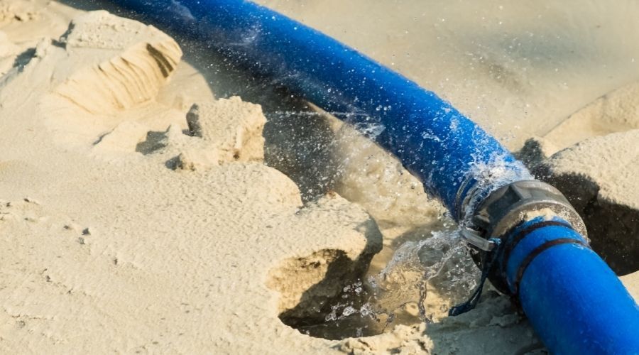a blue garden hose leaking on a surface of sand