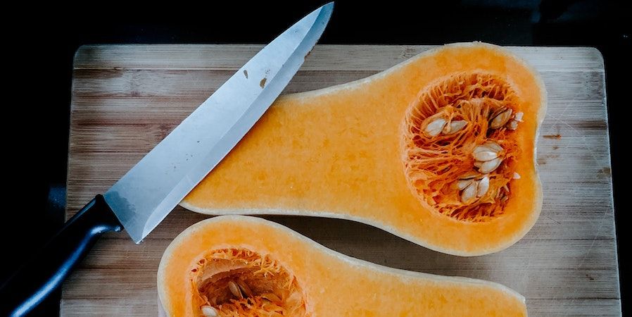 Halved butternut on cutting board with sharp knife 