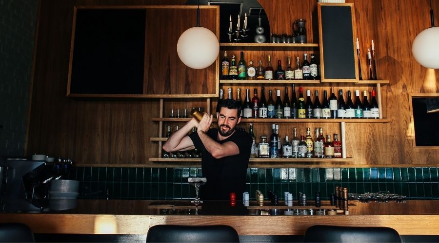 a man mixing a drink behind a wooden bar