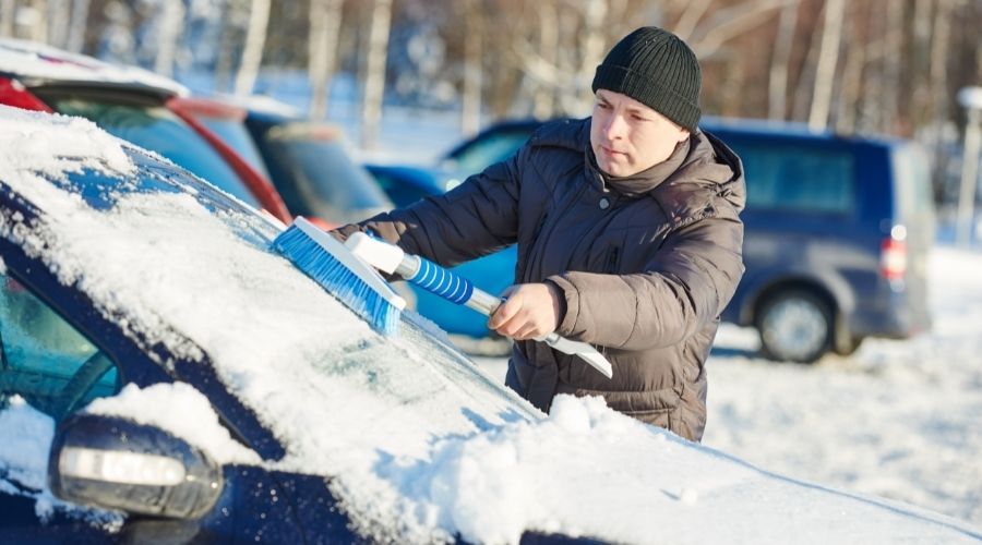 man brushing snow off car