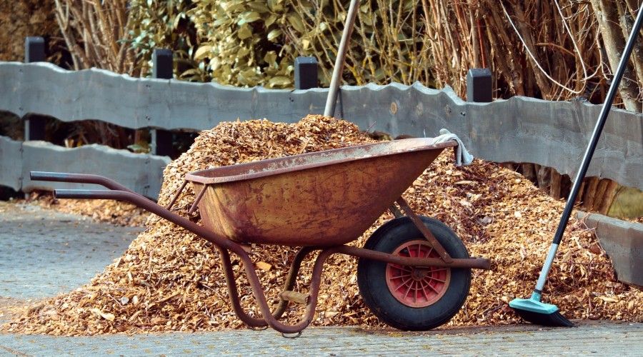 broom and wheelbarrow next to a pile of wood chip mulch