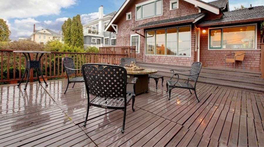 patio furniture on a wooden deck behind a brick house
