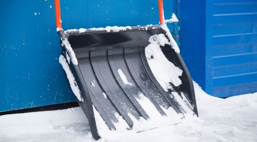 black snow pusher with orange handle leaning against a blue wall