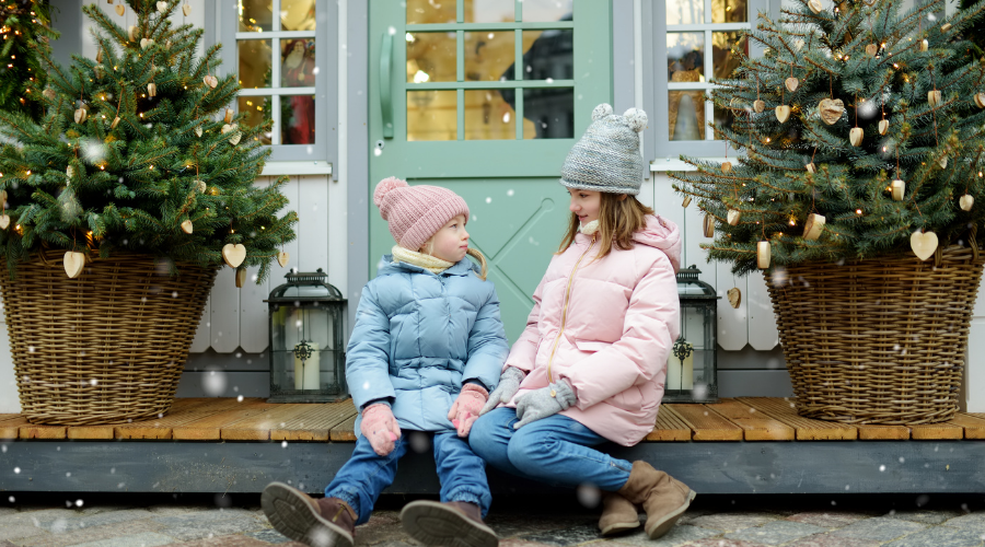 Girls sitting on decorated christmas porch with planters