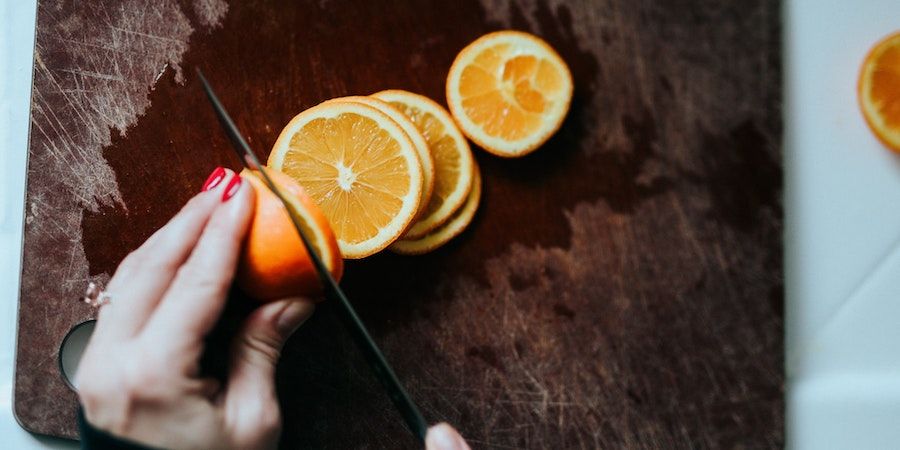 Orange being sliced on a wooden cutting board