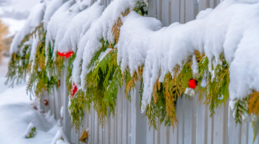 Wooden fence with festive garland covered in snow