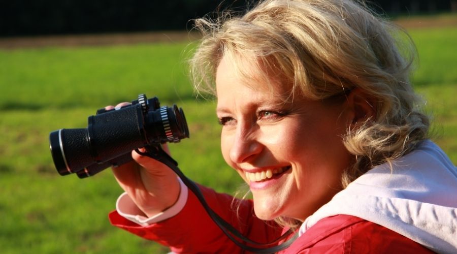 a woman sitting outside smiling while holding binoculars