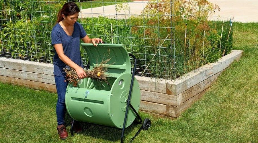 woman putting yard trimmings in a large green compost tumbler