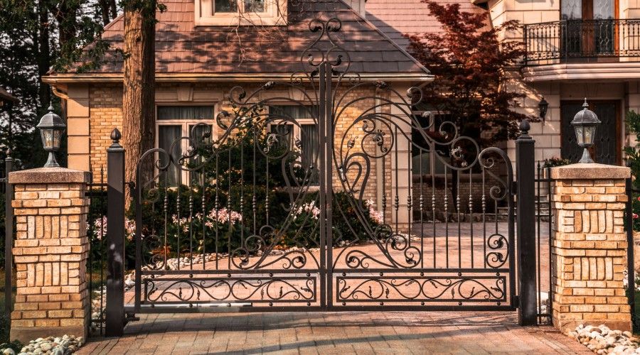 wrought iron driveway entry gate with brick pillars and lights