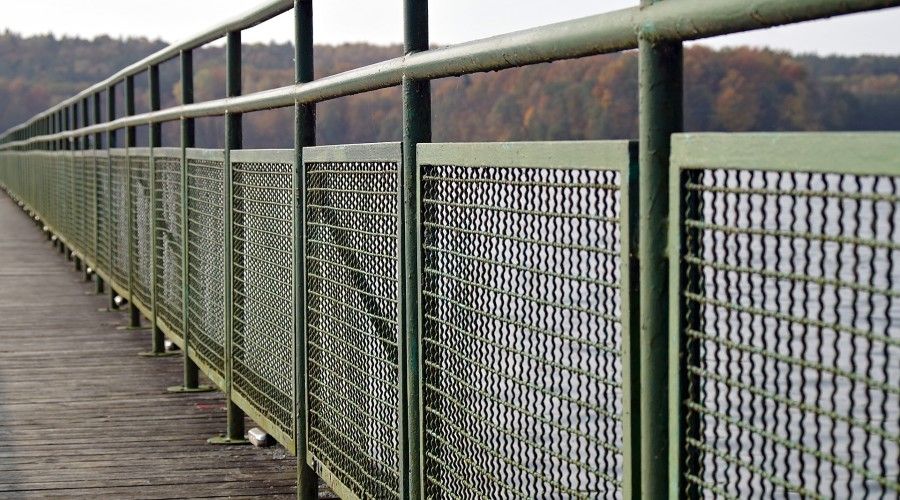 metal fence with metal mesh panels painted green on the side of a bridge