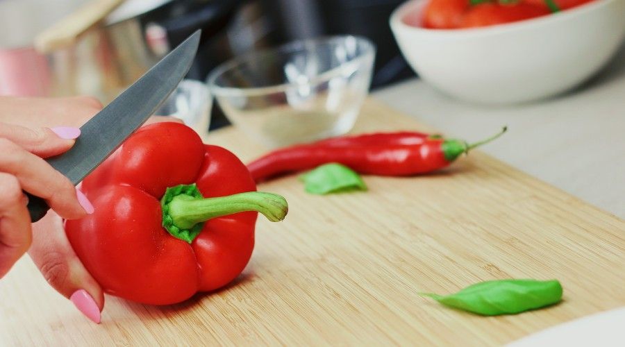 woman cutting a red bell pepper on a wooden cutting board