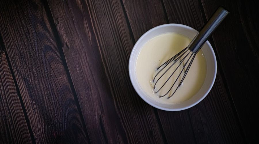 a whisk in a bowl of white batter on a wood backdrop