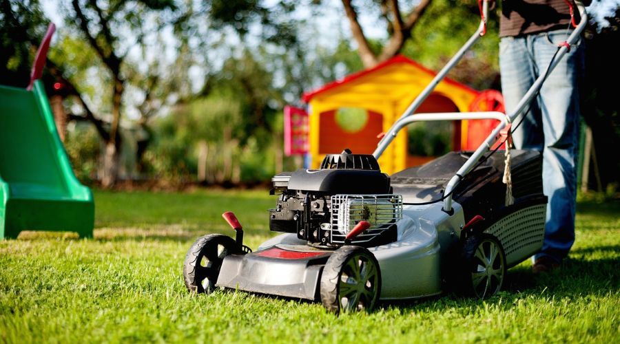 man pushing lawn mower over yard with children's yard toys in background