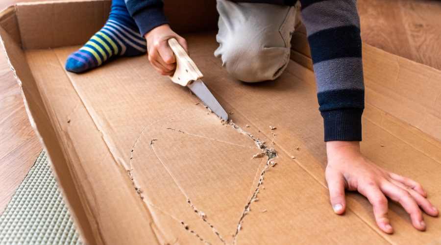 Child Playing with Cardboard Box and Saw