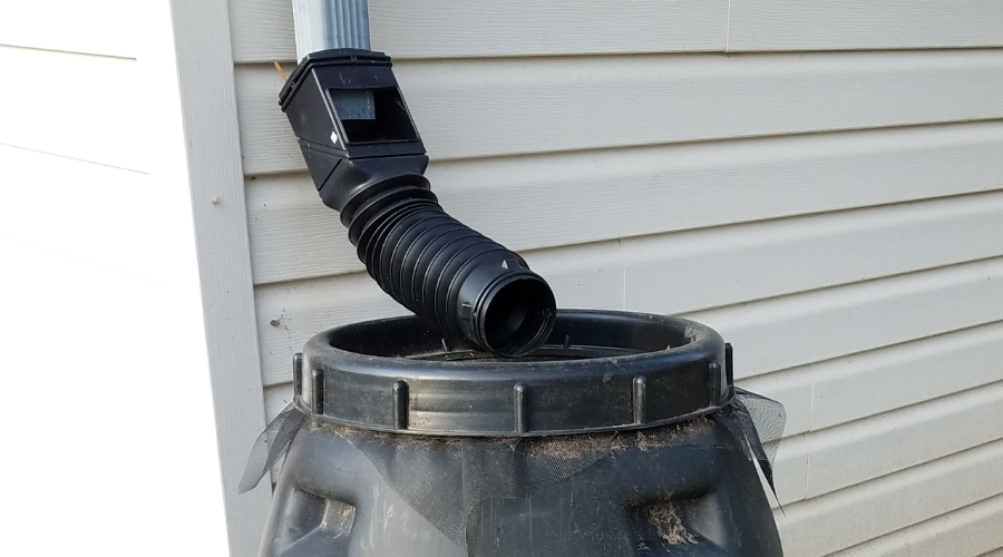 black rain barrel with gutter downspout and hose