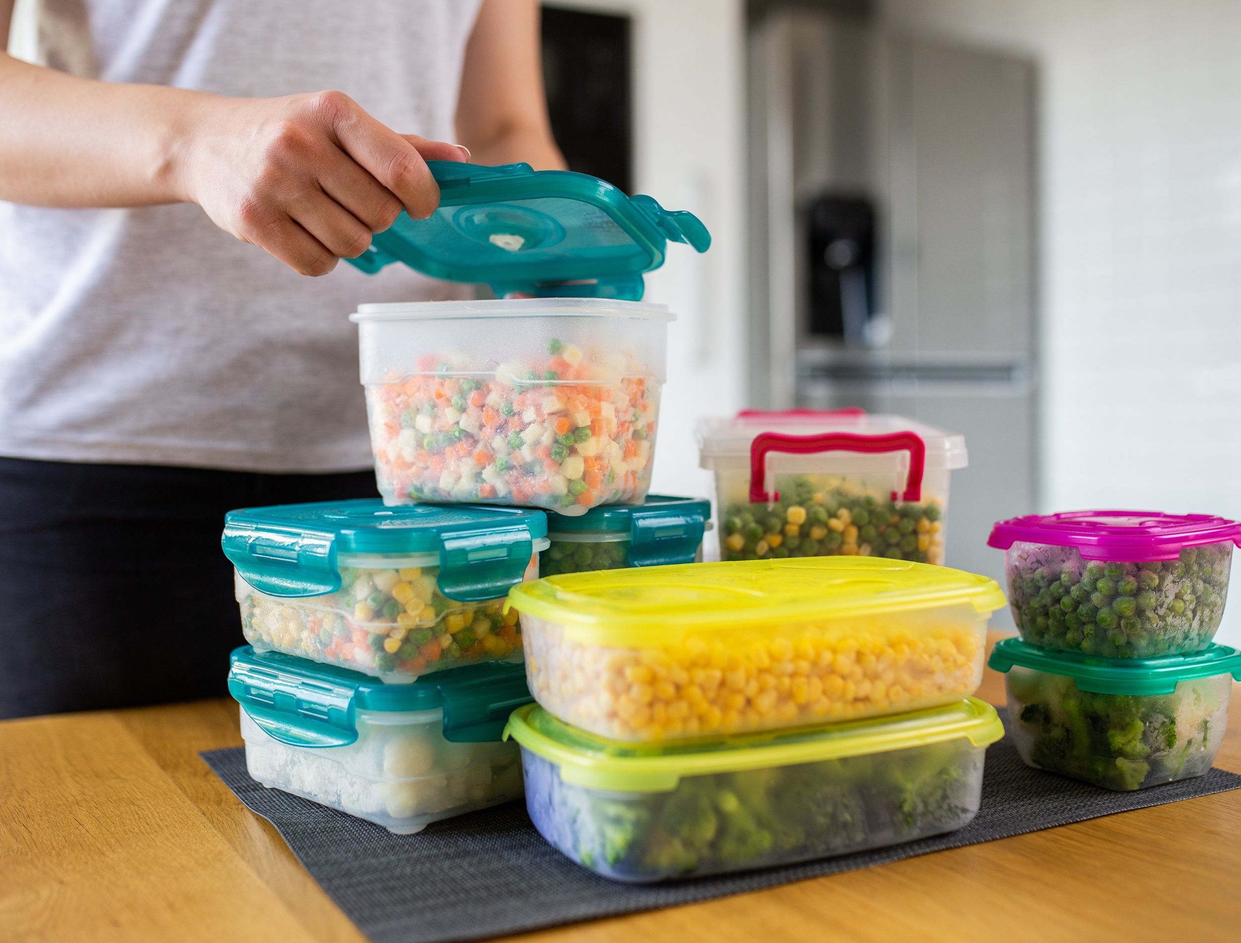 Woman preparing containers with frozen mixed vegetables for refrigerator.