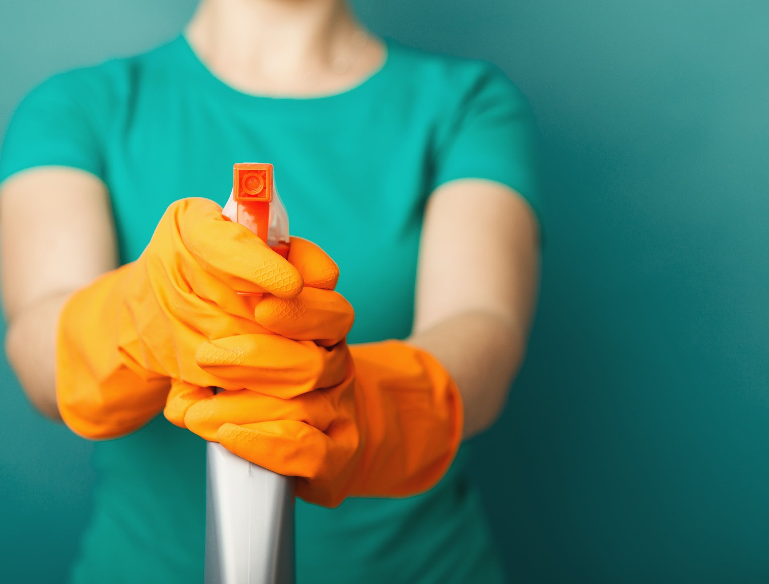 Woman in orange gloves holding a spray of cleaning fluid on blue background, copy space. Household equipment, spring-cleaning, tidying up, cleaning service concept, copy space