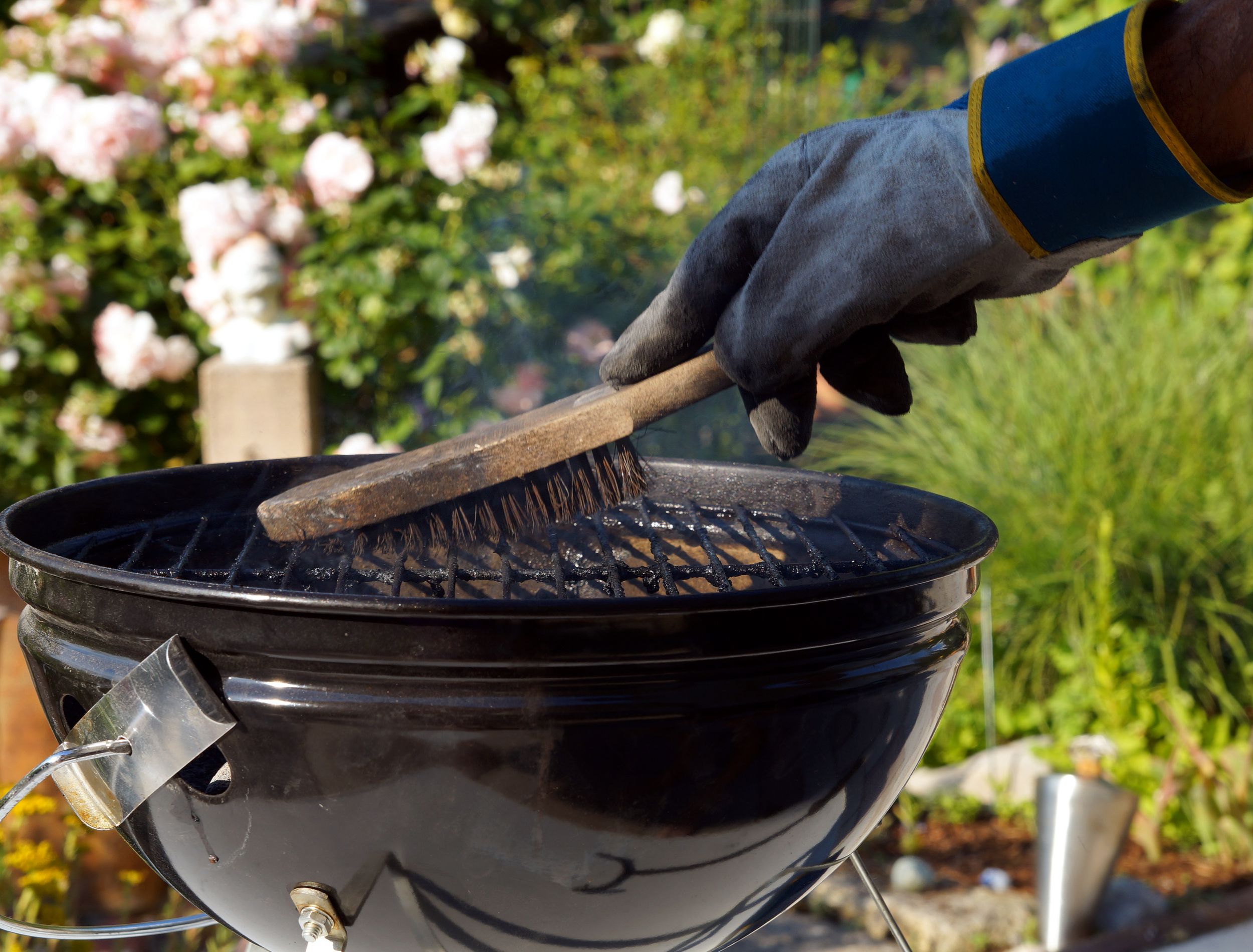 Male hand with gloves cleans round grill with stiff brush