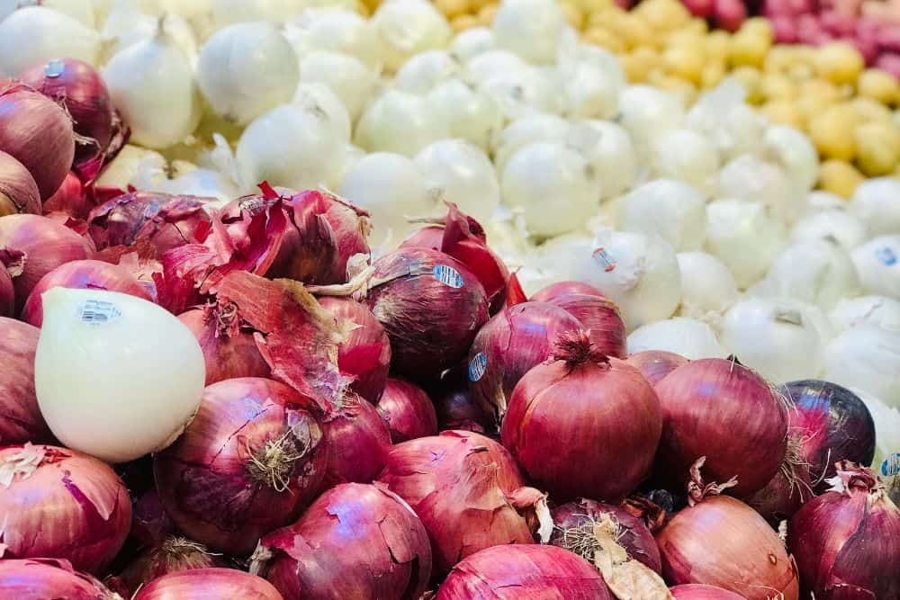 Piles of red onions, white onions, and yellow onions on display
