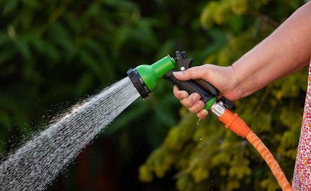 Orange Garden Hose With Green Spray Nozzle Spraying Water