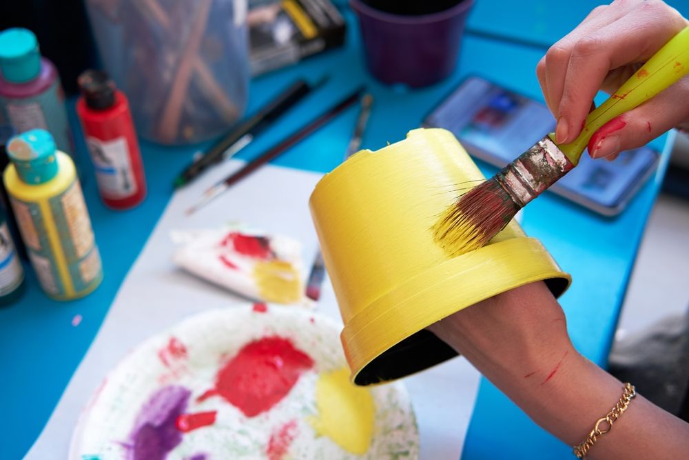Woman hand holding a brush or paintbrush and painting a decorative plastic pot or flowerpot.