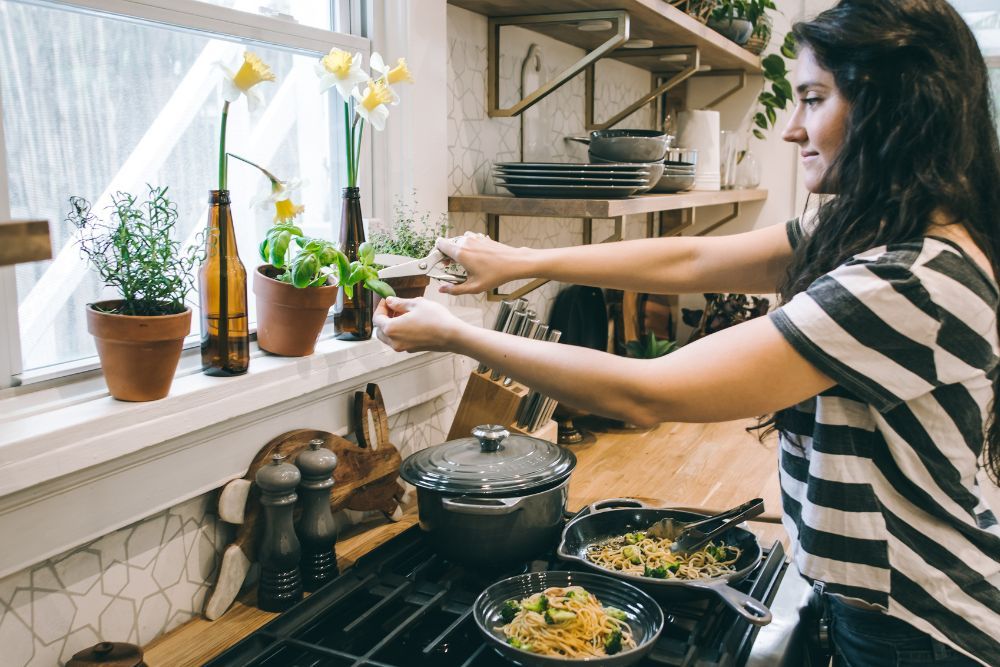 Woman trimming leaves from herb plant sitting in the kitchen windowsill