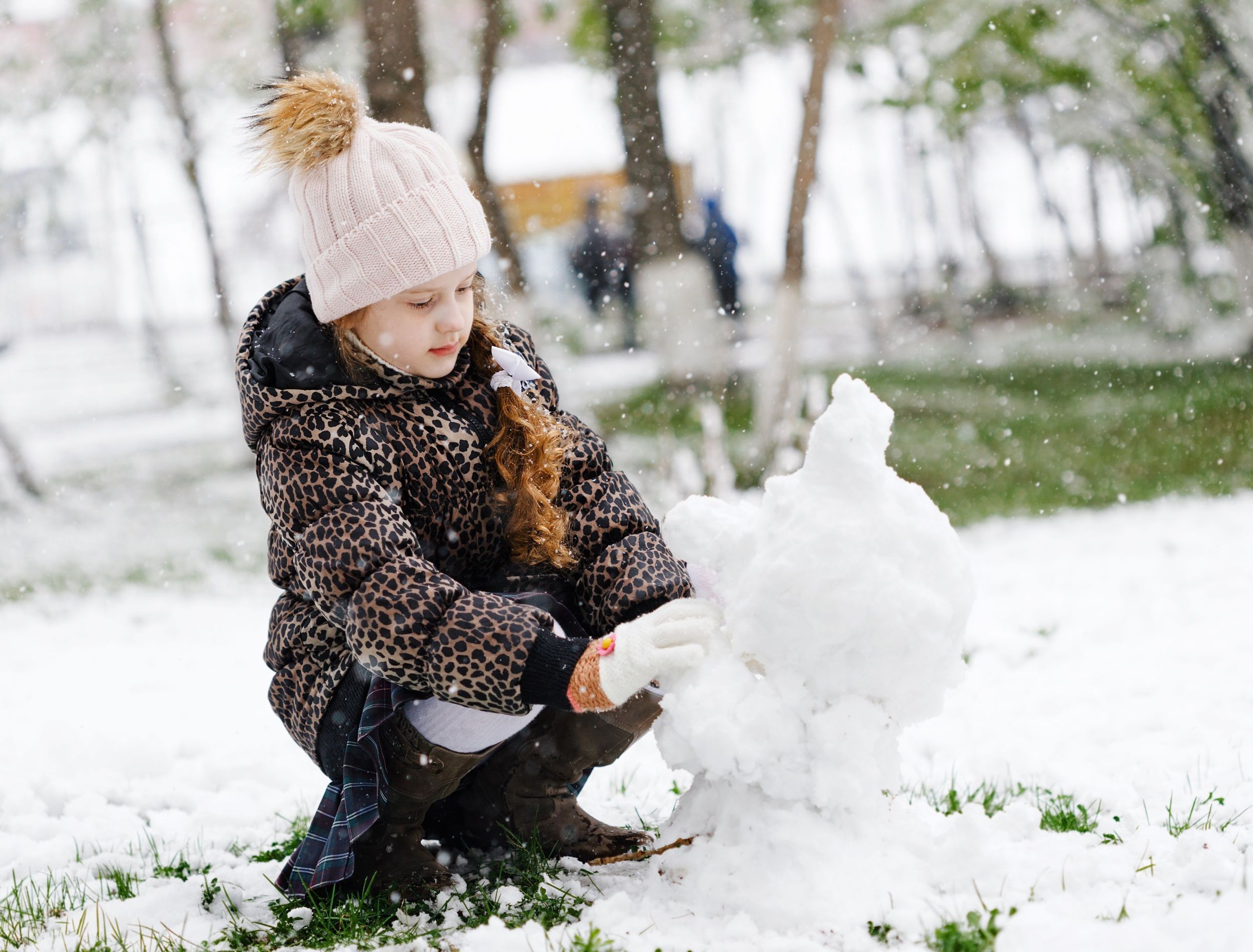 Little girl making snowman on snowy spring day.