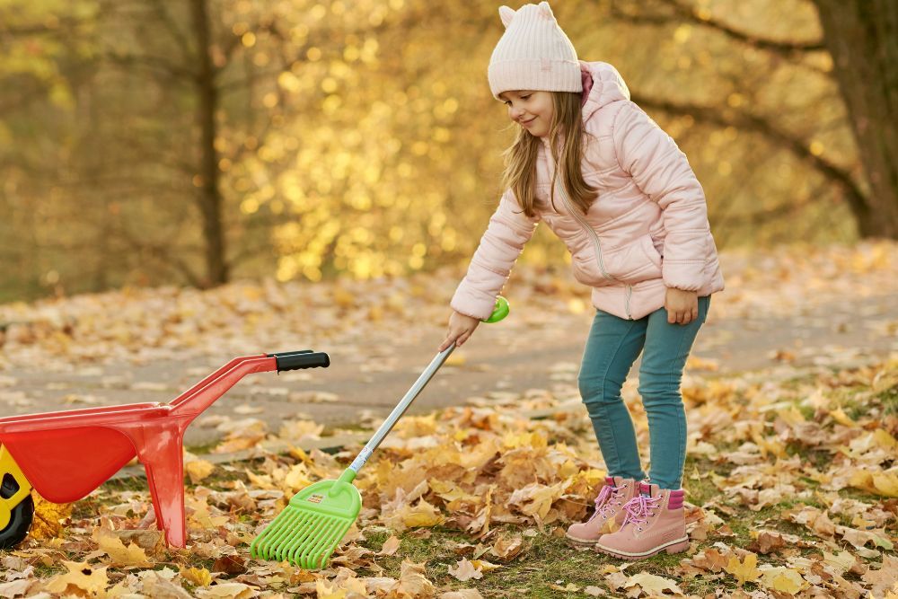 Girl raking leaves on her lawn in autumn