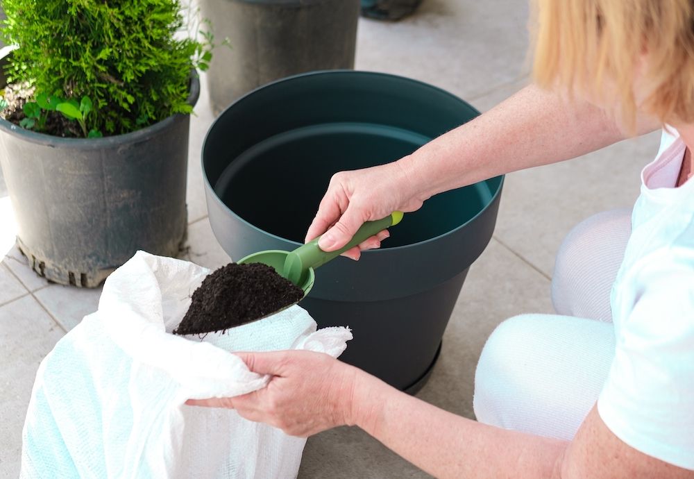 Woman preparing soil for pot planting , working with garden tools