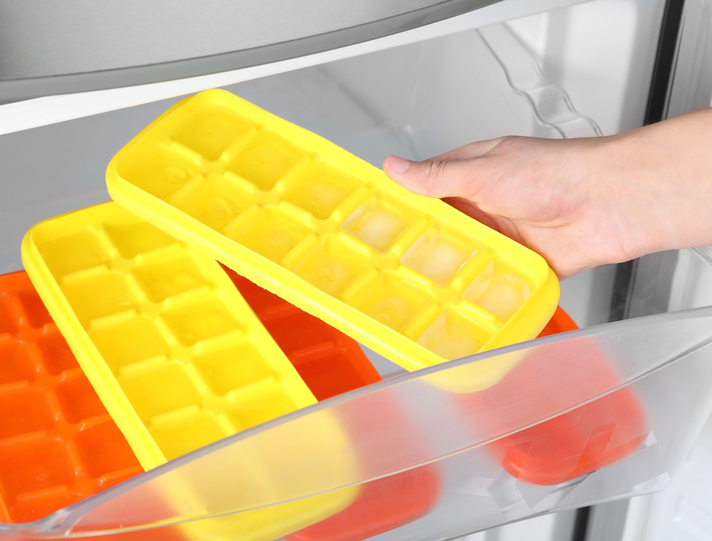 Woman taking tray with ice cubes from fridge, closeup