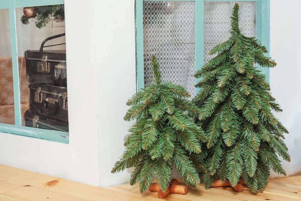 Two small artificial decorative Christmas trees on the porch. Small Christmas trees without ornaments close-up. Fake Christmas tree decor on the window background