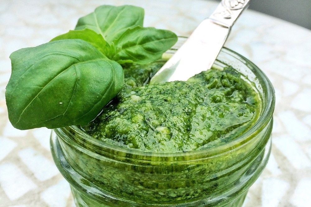 basil pesto in glass jar with metal spoon and basil sprig on top