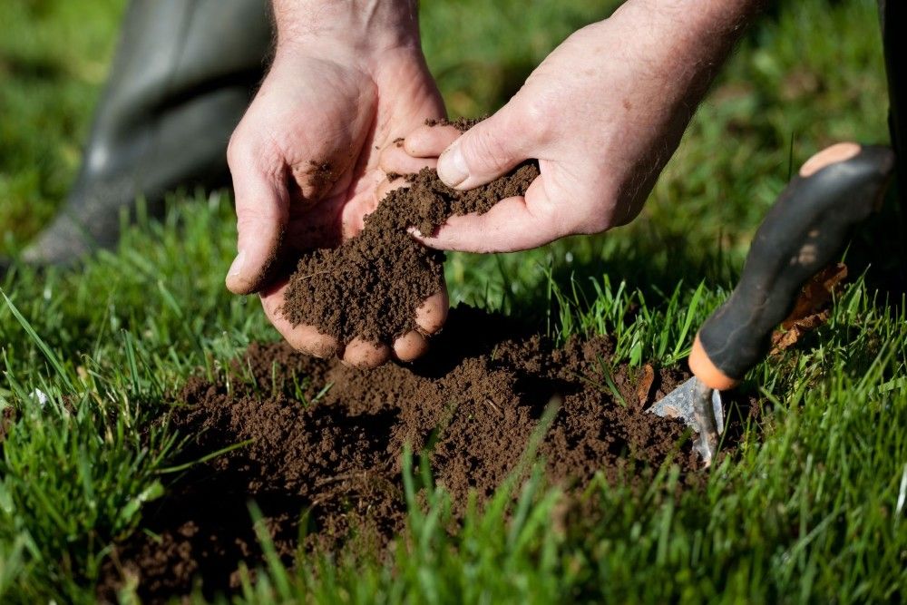 person feeling the soil with grass and shovel at their feet