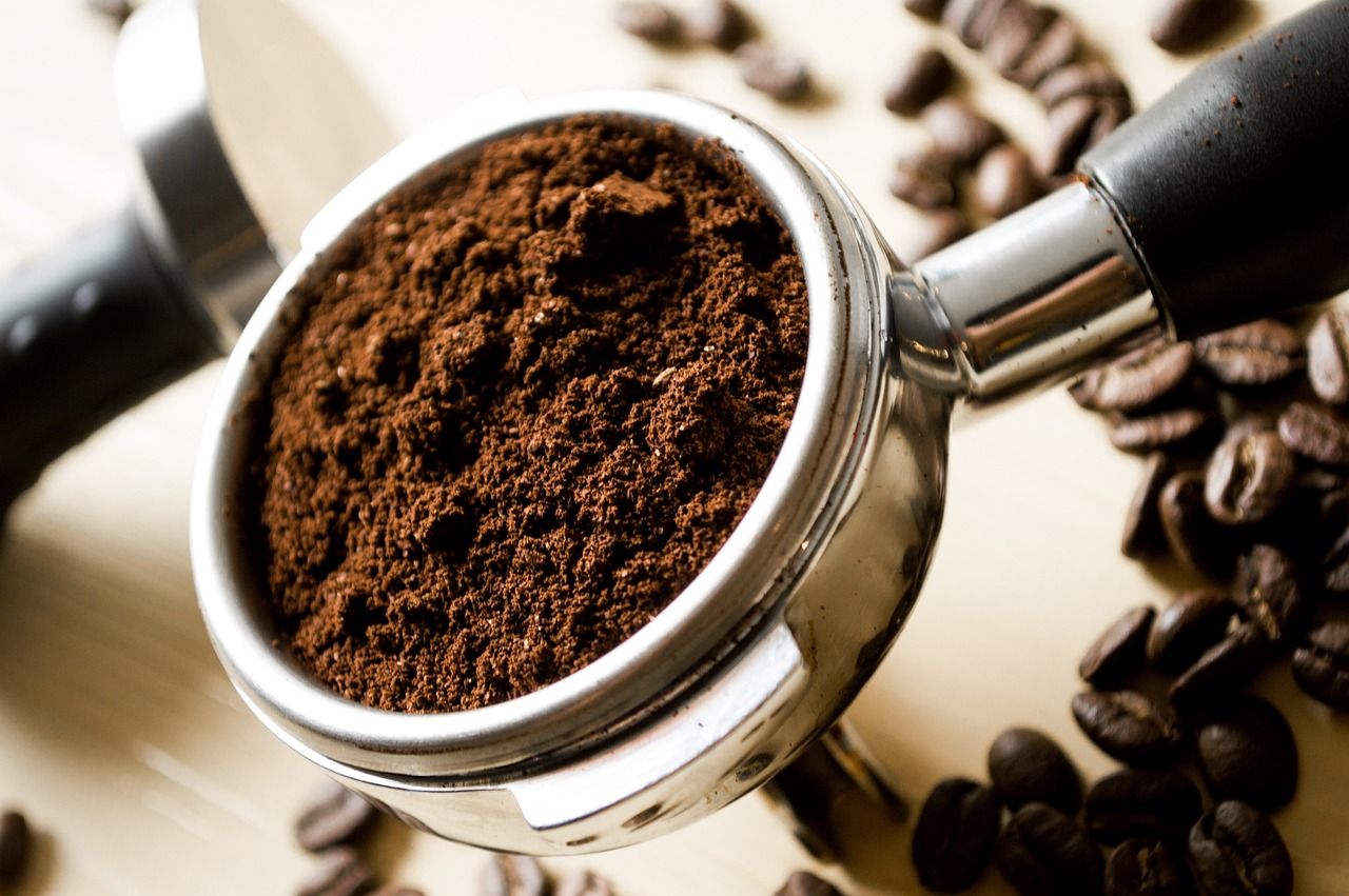 coffee grounds in a small steel container with beans in background