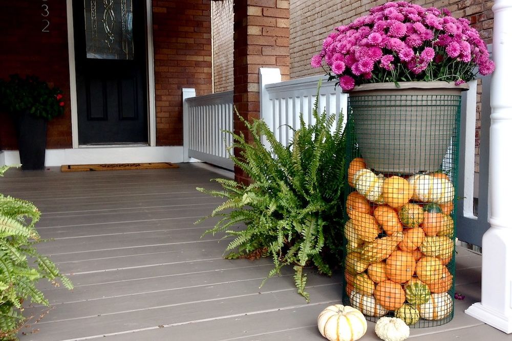 A DIY plant stand filled with flowers and pumpkins on a porch.