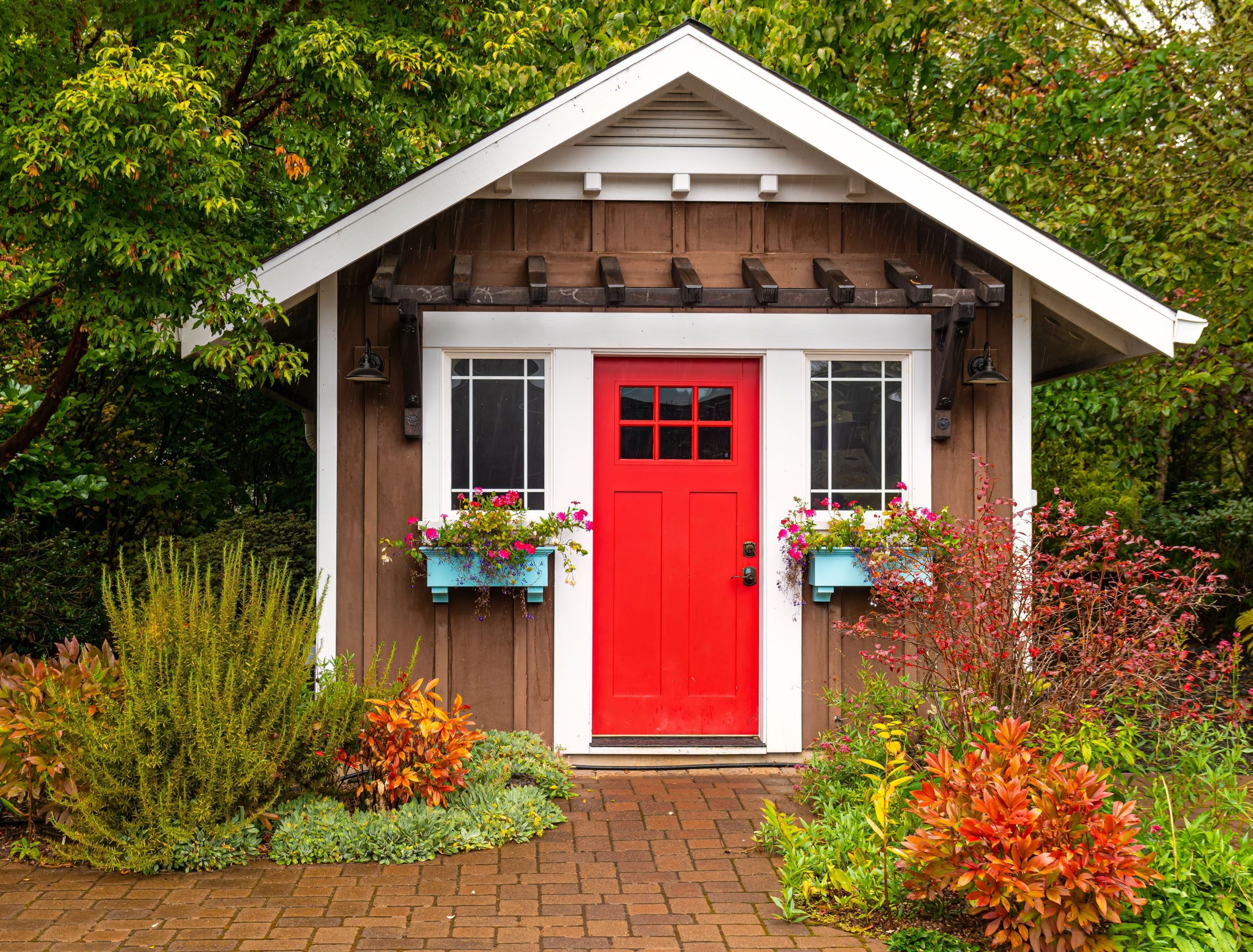Small colorful wooden garden shed with a red door and window baskets of flowers.