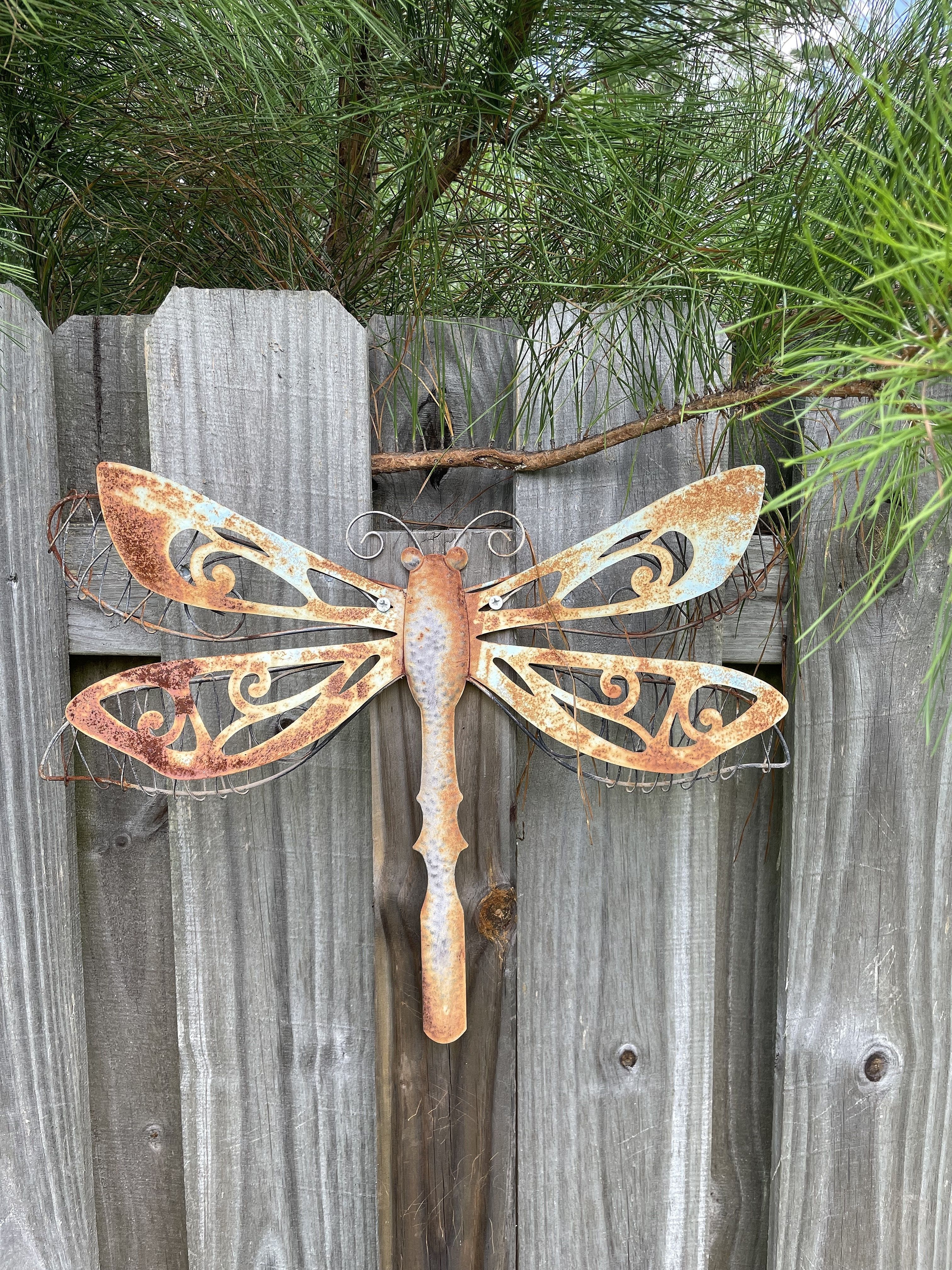 A large rusty metal dragonfly attached to a light brown fence as backyard decoration.