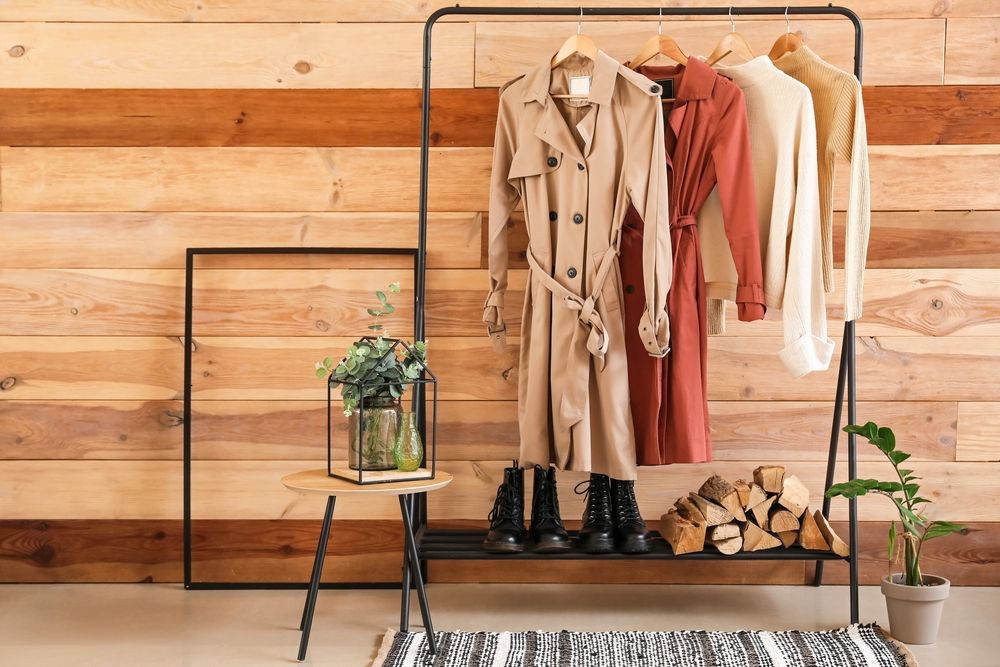 Rack with clothes and firewood near wooden wall