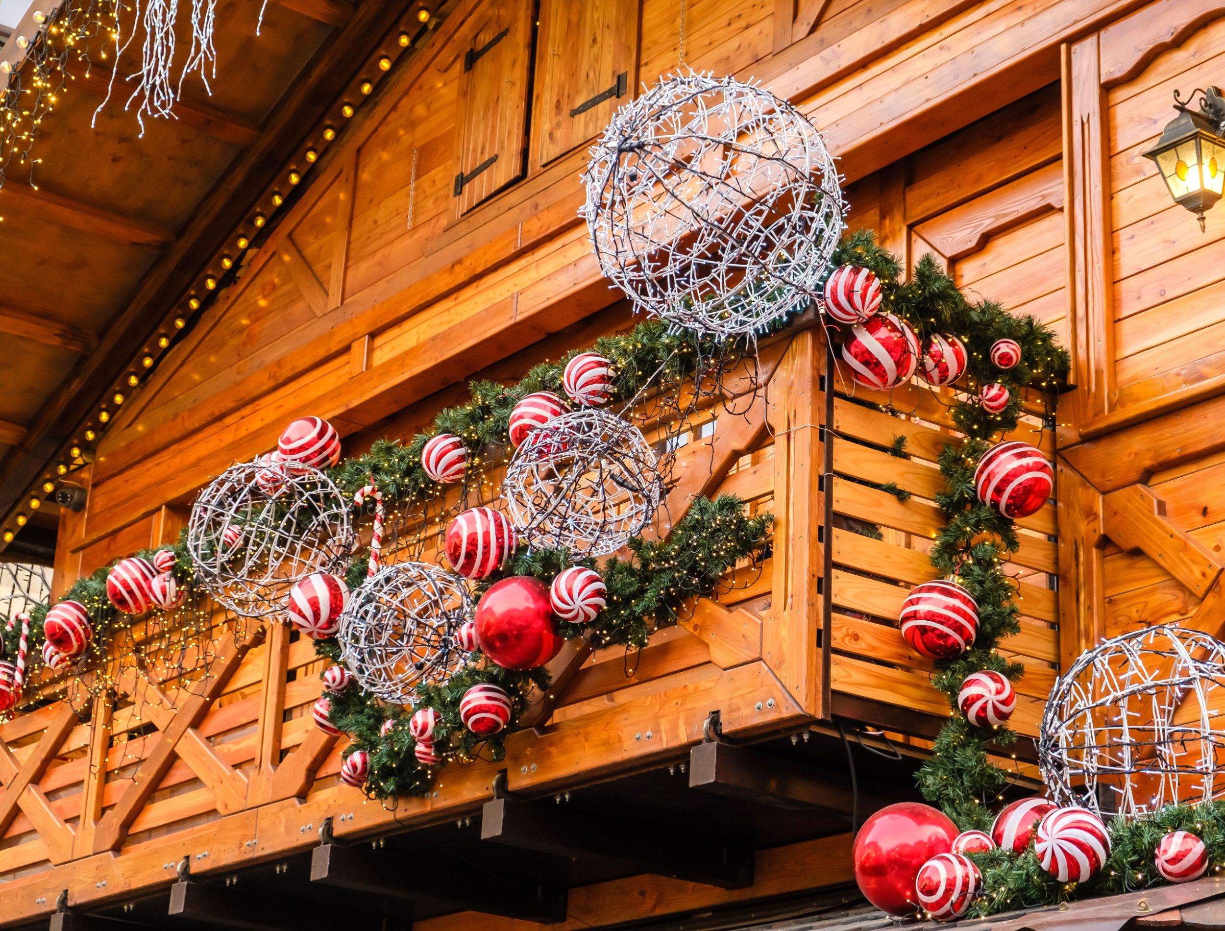 Balcony of Wooden Vintage Building Decorated of Artificial Fir Tree with Garland and many Red and White Christmas Balls at Winter Day, no Snow.