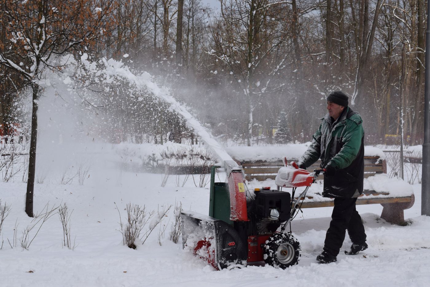 A person with a green jacket using a snow blower