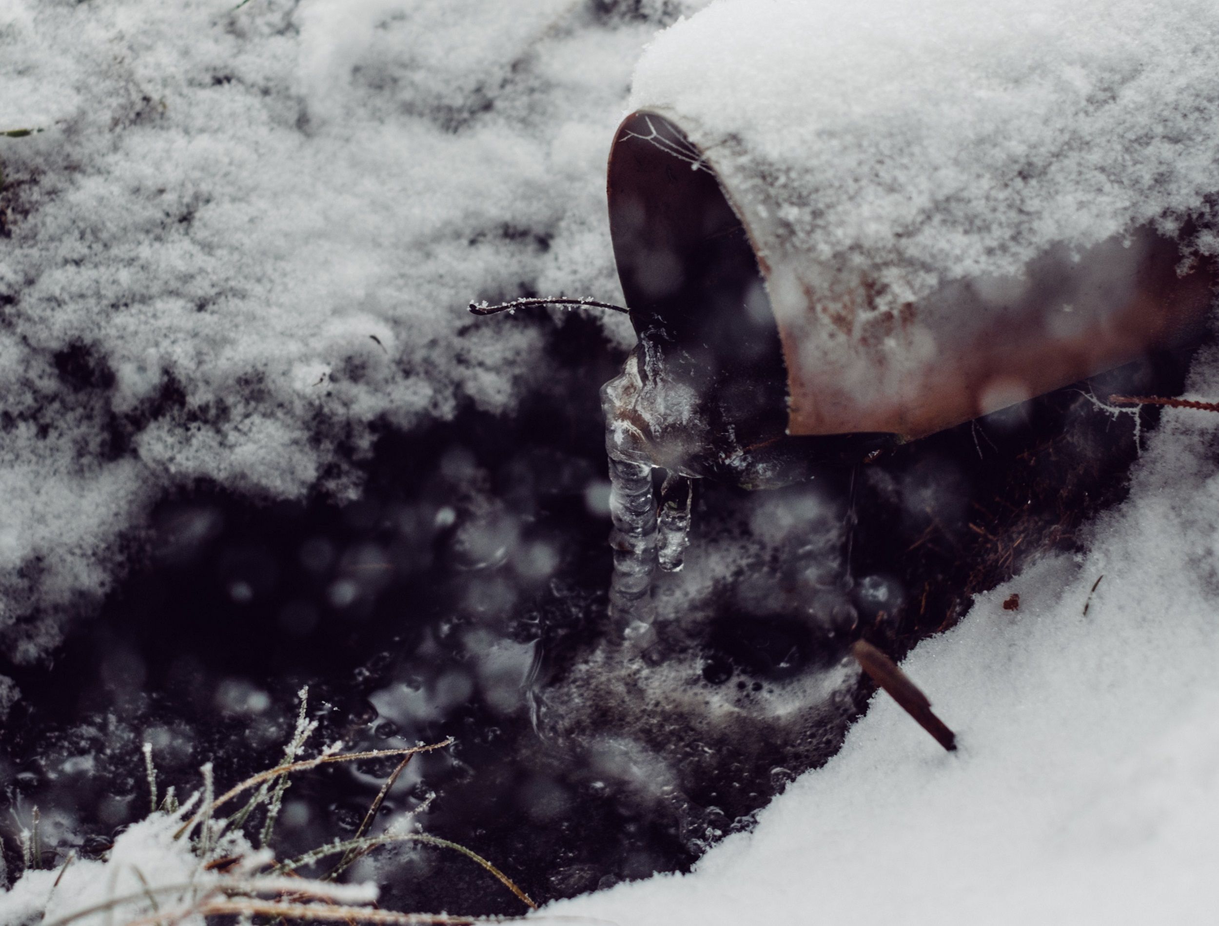 Drain pipe in the snow with icicles and slush