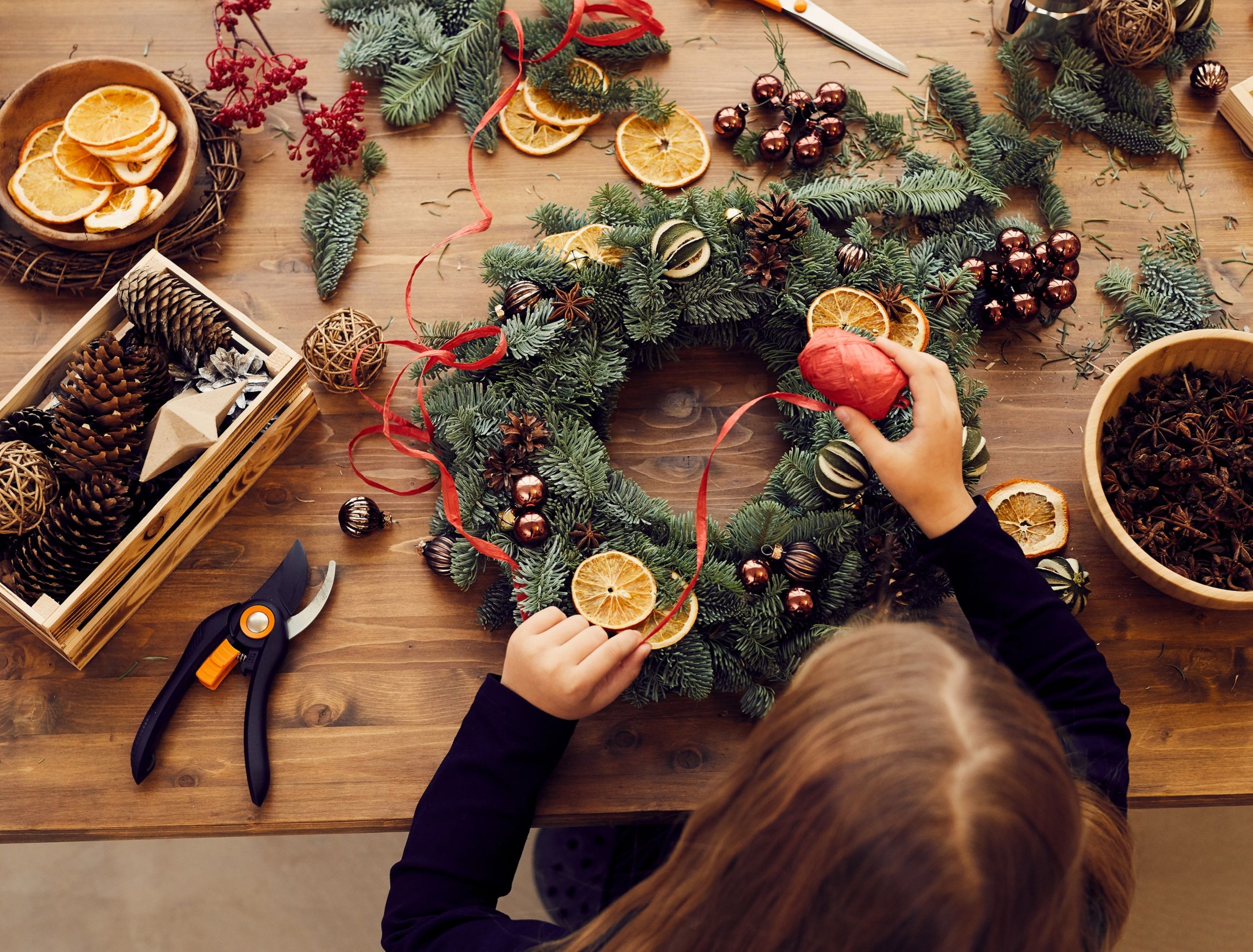 Making a DIY winter wreath with materials on table and person constructing