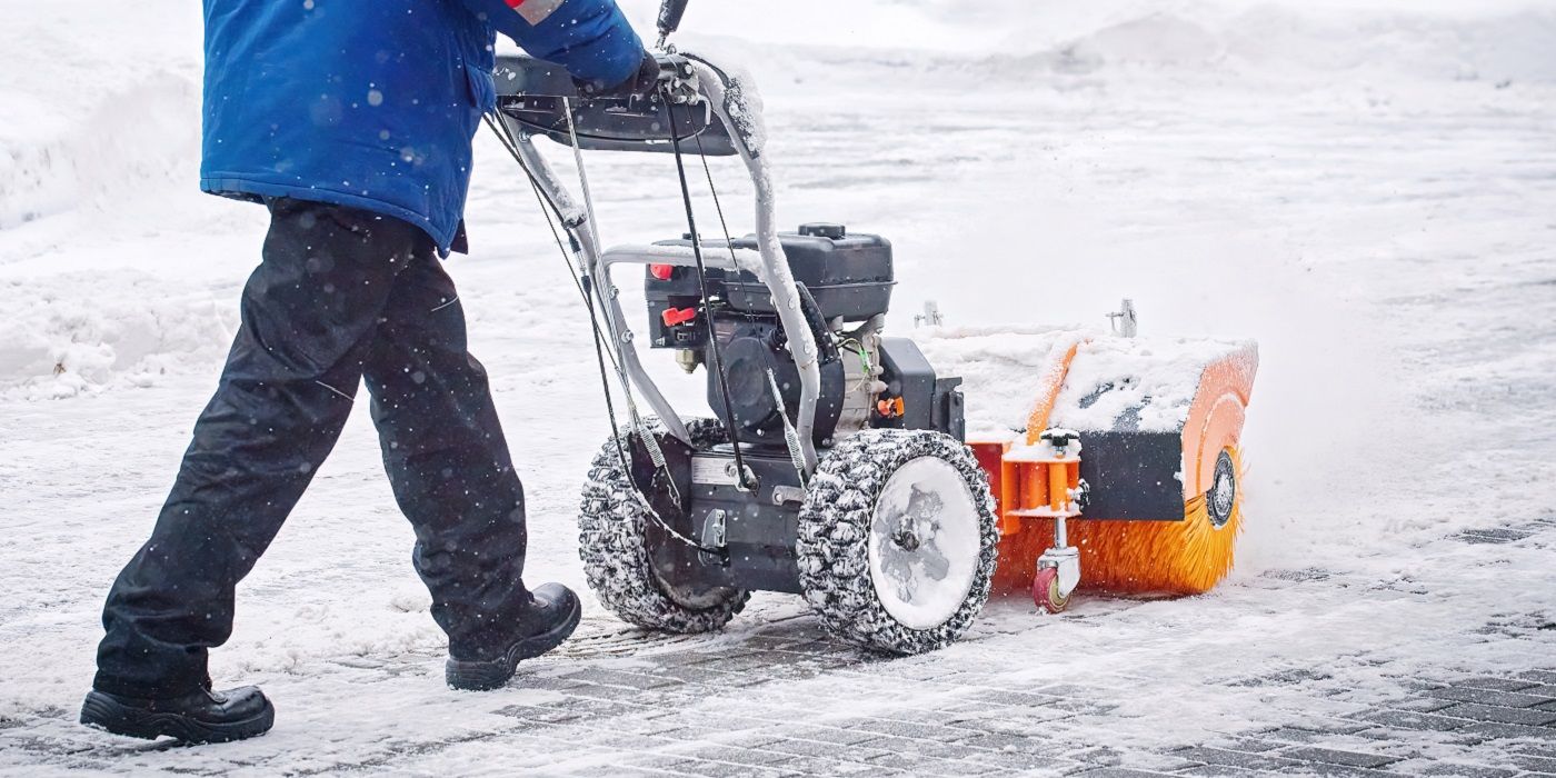 Person using a power brush snow sweeper outside