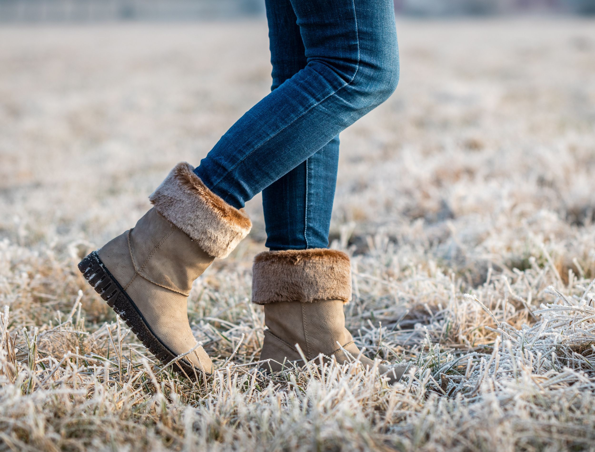 Person wearing winter boots walking across icy frosty grass on a winter lawn