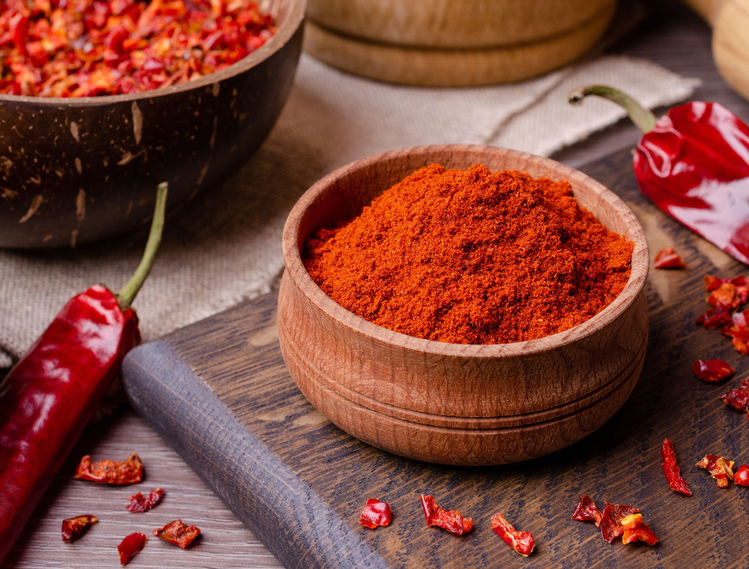 Cayenne pepper powder in wooden bowl surrounded by peppers