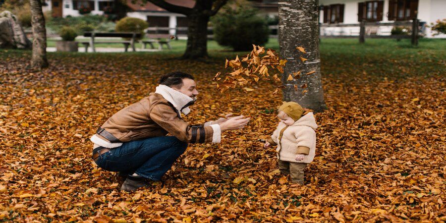 Father and child on a lawn covered in fallen leaves.