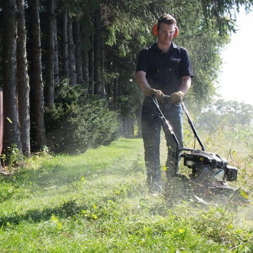 A homeowner cutting an overgown lawn with a wheeled string timmer.