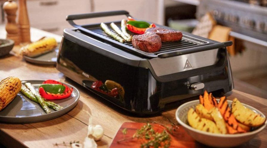 A Philips infrared grill standing on a kitchen table with grilled BBQ sides next to it.