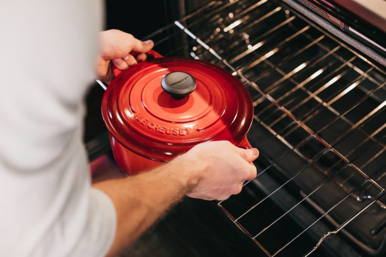 A man putting a red dutch oven into the oven